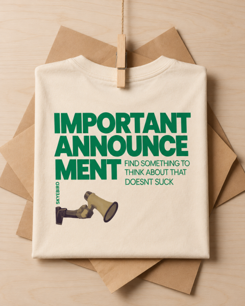 Folded cream T-shirt with green “Important Announcement: Find something to think about that doesn’t suck” lettering and a megaphone.