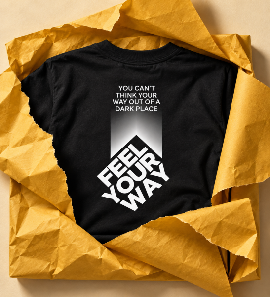 Black T-shirt in yellow wrapping paper reading “You can’t think your way out of a dark place” and “Feel your way”.