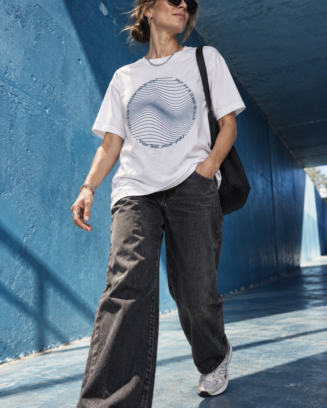 Woman wearing a white You Don’t Think Your Way T-shirt beside a blue wall.