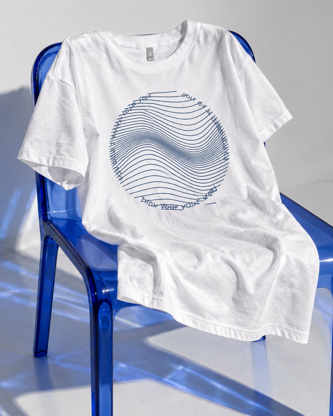 White You Don’t Think Your Way T-shirt with circular blue wave artwork draped over a blue chair.