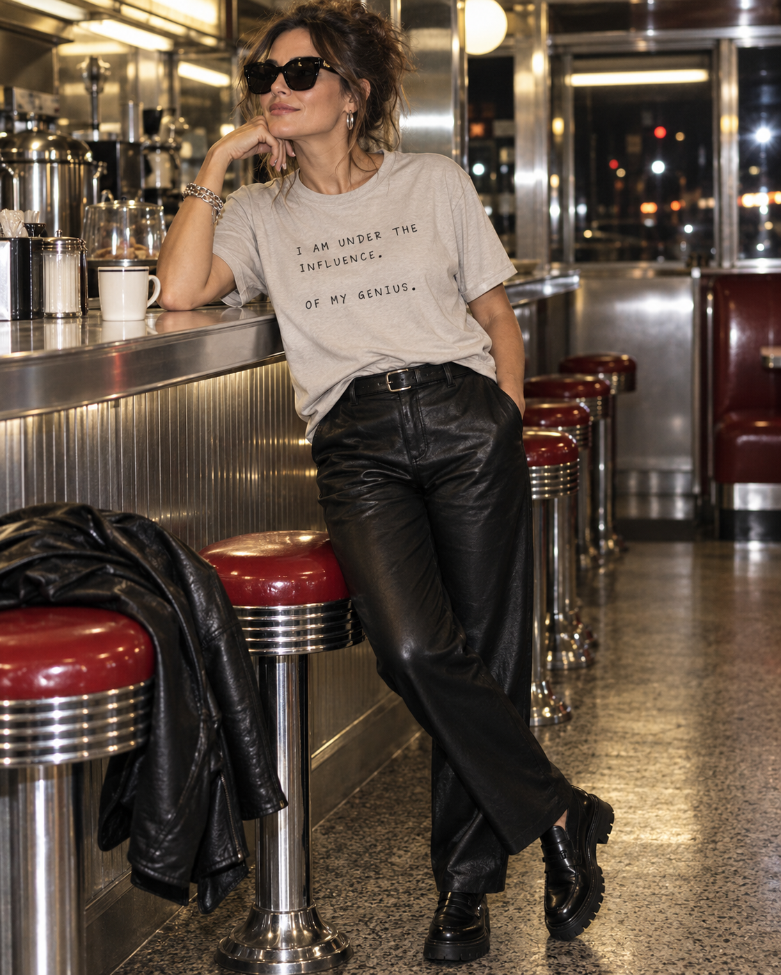 Woman in a light grey Under the Influence of My Genius T-shirt at a chrome diner counter.